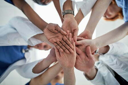 Diverse group of people with hands placed in centre of the group | HQCA